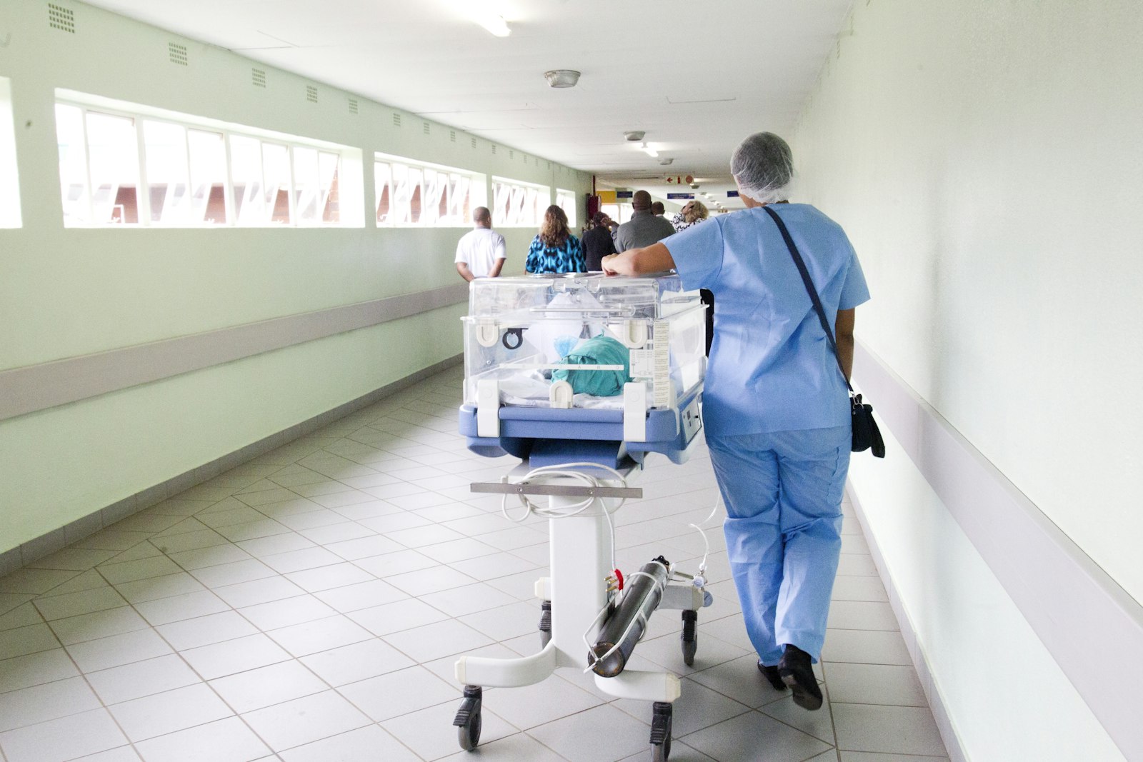 A healthcare worker moving equipment along a ward corridor